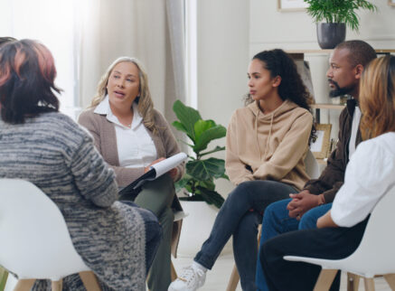 A group of people sitting in a circle listening to a woman talk