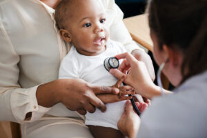 African american baby sitting in a lap while a nurse checks her heartbeat