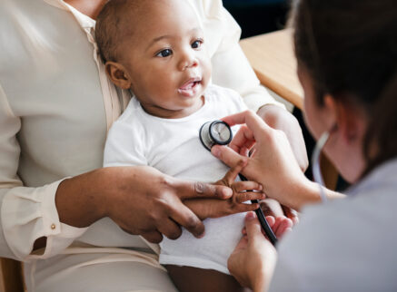 African american baby sitting in a lap while a nurse checks her heartbeat