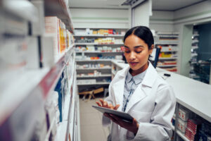 Pharmacist looking at a tablet in front of a row of prescriptions