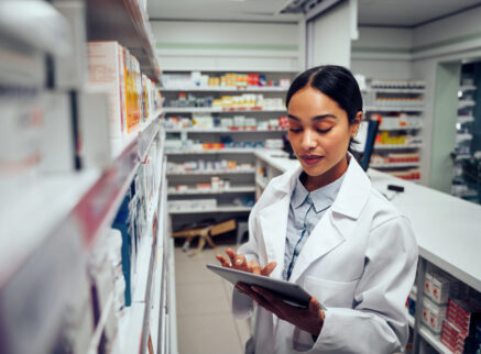 Pharmacist looking at a tablet in front of a row of prescriptions